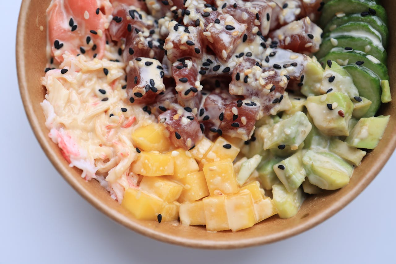 about-us Colorful poke bowl featuring tuna, avocado, mango, and cucumbers with sesame garnish.